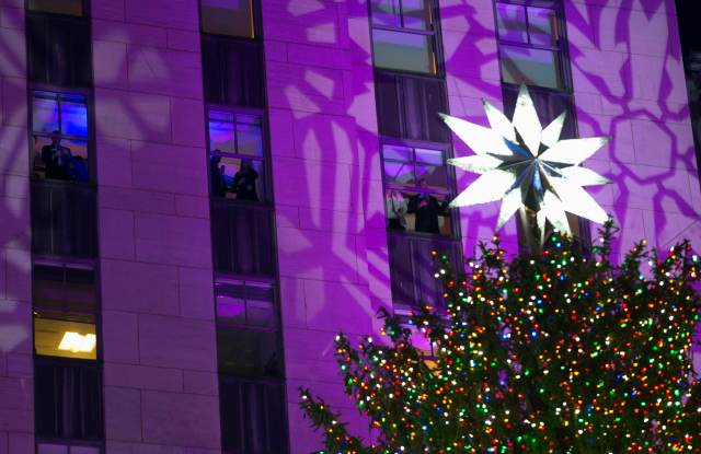 People look out from windows from the 30 Rockefeller Center building, at the 82nd Rockefeller Center Christmas tree shortly after being lit at the annual ceremony in midtown Manhattan in New York City