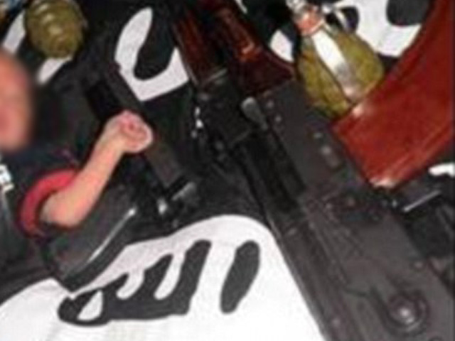 Terroristas colocan a un bebé con armas sobre la bandera del Estado Islámico