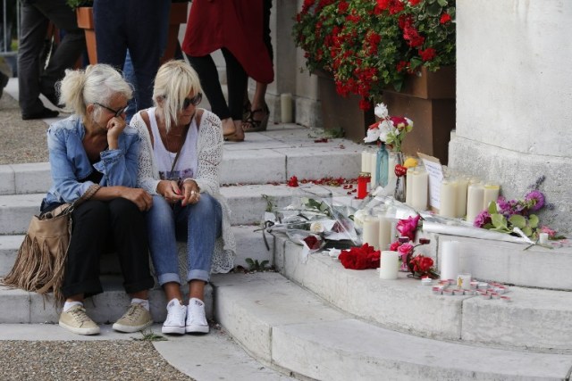 Two women sit near candles and flowers displayed in front of the city hall of the Normandy city of Saint-Etienne du Rouvray on July 26, 2016 after a priest was killed in the latest of a string of attacks against Western targets claimed by or blamed on the Islamic State jihadist group. French President said that two men who attacked a church and slit the throat of a priest had "claimed to be from Daesh", using the Arabic name for the Islamic State group. Police said they killed two hostage-takers in the attack in the Normandy town of Saint-Etienne-du-Rouvray, 125 kilometres (77 miles) north of Paris. / AFP PHOTO / MATTHIEU ALEXANDRE