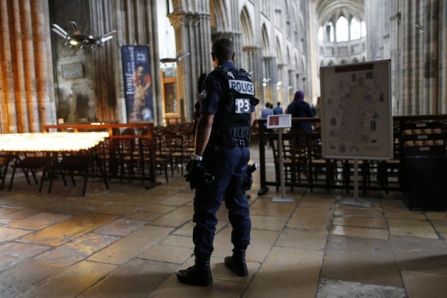 A policeman stands guard while people arrive for a Mass at the Rouen Cathedral, on July 27, 2016 in Rouen, to pay tribute to the priest Jacques Hamel, killed on July 26 in a church of Saint-Etienne-du-Rouvray during a hostage-taking claimed by Islamic State group. France probes an attack on a church in which two men described by the Islamic State group as its "soldiers" slit the throat of a priest. An elderly priest had his throat slit in a church in northern France on July 26 after two men stormed the building and took hostages. The attack in the Normandy town of Saint-Etienne-du-Rouvray came as France was still coming to terms with the Bastille Day killings in Nice claimed by the Islamic State group. / AFP PHOTO / CHARLY TRIBALLEAU