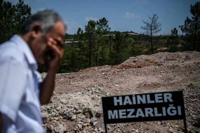 A man stays next to a sign reading in Turkish language "Traitors' Cemetery" is seen in front of unmarked graves built specially by Istanbul municitality for the dead failed coup soldiers, on July 28,2016 at Pendik district in Istanbul. Turkey's top military commanders met Thursday to replace almost half of their generals in a radical shake-up after the failed coup, as authorities shut down dozens of media outlets in a widening crackdown. / AFP PHOTO / OZAN KOSE