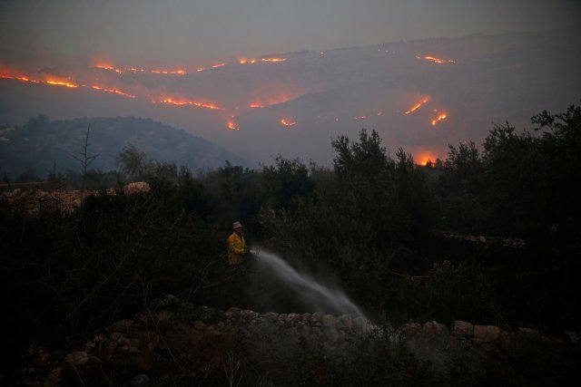 A firefighter sprays water around a house in Nataf as wildfire burns on the hills and mountains around it, outside Jerusalem November 25, 2016.  REUTERS/Ammar Awad     TPX IMAGES OF THE DAY