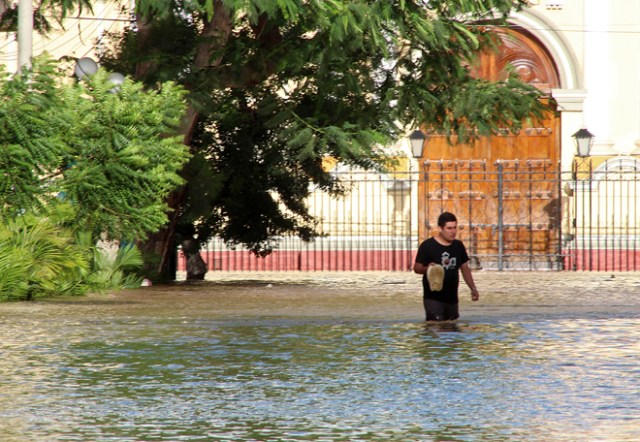 Residents in the city of Piura, 1,000 kilometres north of Lima, wade through water on the streets on March 27, 2017, after nearly 15 hours of rain caused the Piura River to overflow, flooding neighbourhoods in most of the city.  The El Nino climate phenomenon is causing muddy flash floods and rivers to overflow along the entire Peruvian coast, isolating communities and neighborhoods. Most cities face water shortages as water lines have been compromised by mud and debris. / AFP PHOTO / PATRICIA LACHIRA