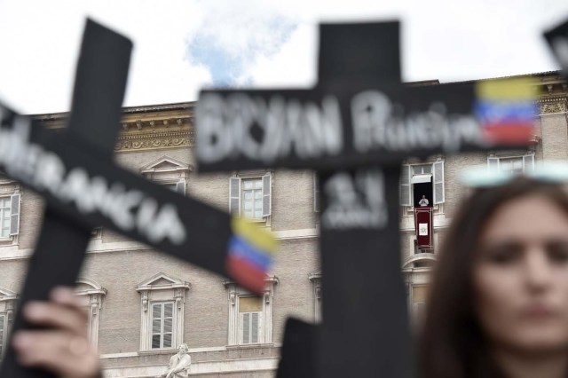 Members of the Venezuelian community hold black crosses with names of victims of clashes during protests against Venezuela's President Nicolas Maduro, on May 7, 2017 at St Peter's square as Pope Francis stands at the window of the apostolic palace during the Regina Coeli prayer in Vatican. Pope Francis last week made a heartfelt appeal for "negotiated solutions" to end the violence in crisis-torn Venezuela for the sake of an "exhausted population".  The death toll since April -- when the protests intensified after Maduro's administration and the courts stepped up efforts to undermine the opposition -- is at least 36, according to prosecutors, with hundreds more injured. / AFP PHOTO / TIZIANA FABI