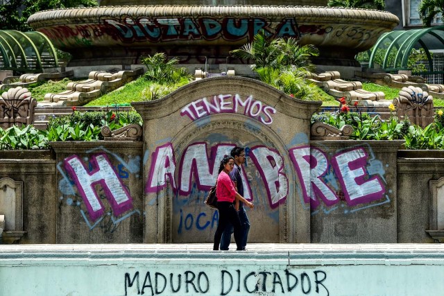 A couple walks by graffitis reading "We Are Hungry" and "Maduro Dictator" in Caracas on August 8, 2017. Recent demonstrations in Venezuela have stemmed from anger over the installation of an all-powerful Constituent Assembly that many see as a power grab by the unpopular President Nicolas Maduro. The dire economic situation also has stirred deep bitterness as people struggle with skyrocketing inflation and shortages of food and medicine.  / AFP PHOTO / Ronaldo SCHEMIDT