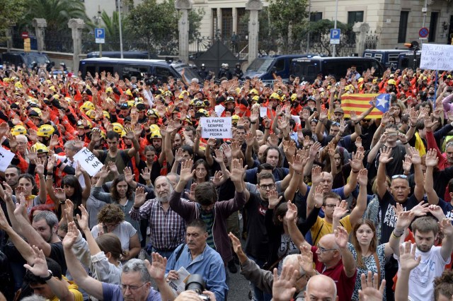 Protesters joined by firefighters raise their hands as they gather during a general strike in Barcelona called by Catalan unions on October 3, 2017. Large numbers of Catalans are expected to observe a general strike today to condemn police violence at a banned weekend referendum on independence, as Madrid comes under growing international pressure to resolve its worst political crisis in decades. / AFP PHOTO / Josep LAGO