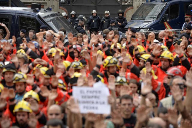 Police forces stand guard as firefighters raise their hands during a general strike in Barcelona called by Catalan unions on October 3, 2017. Large numbers of Catalans are expected to observe a general strike today to condemn police violence at a banned weekend referendum on independence, as Madrid comes under growing international pressure to resolve its worst political crisis in decades. / AFP PHOTO / Josep LAGO