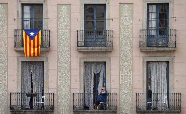 A Catalan flag hangs from a balcony as a woman watches a demonstration in a square in Barcelona, Spain, October 7, 2017 REUTERS/Eric Gaillard
