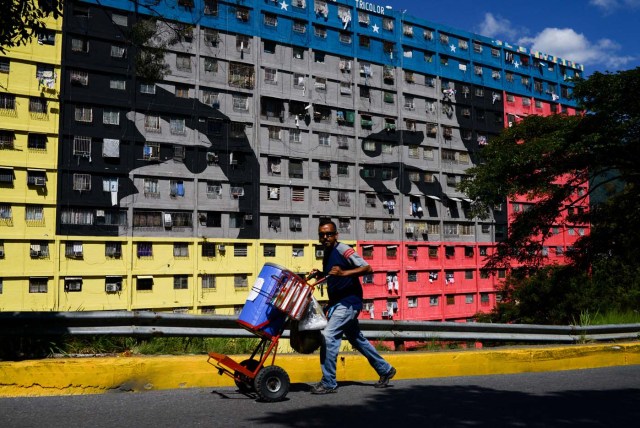 Un hombre empuja una carreta en la calle frente a un edificio que representa los ojos del difunto presidente venezolano Hugo Chávez en el vecindario" 23 de Enero "en Caracas el 15 de diciembre de 2017. 