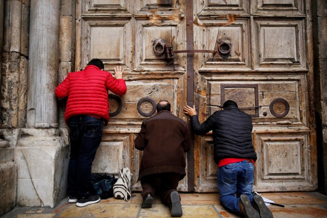 Fieles arrodillados rezan frente a la puerta cerrada de la Iglesia del Santo Sepulcro en la Ciudad Antigua de Jerusalén, 25 de febrero de 2018. REUTERS/Amir Cohen.