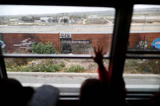 Members of a caravan of migrants from Central America ride on a bus past the border fence between Mexico and the U.S., to gather in a park prior to preparations for an asylum request in the U.S., in Tijuana, Mexico April 29, 2018. REUTERS/Edgard Garrido
