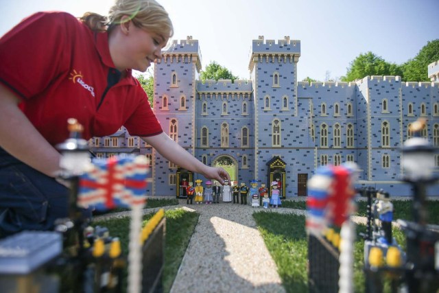 Legoland employee, Lucy, poses putting a Lego model of US actress Meghan Markle (C) in place next to her husband-to-be Britain's Prince Harry along with their families outside a Lego-brick model of Windsor Castle at Legoland in Windsor on May 8, 2018 during a photo call for its attraction celebrating the upcoming royal wedding. Prince Harry and US actress Meghan Markle will marry on May 19 at St. George's Chapel at Windsor Castle. / AFP PHOTO / Daniel LEAL-OLIVAS