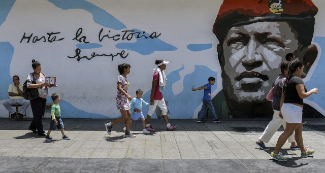 La gente camina por un graffiti con una imagen del difunto presidente Hugo Chávez en Caracas el 11 de mayo de 2018. Los ciudadanos venezolanos enfrentarán elecciones presidenciales el 20 de mayo en medio de una severa crisis socioeconómica, con hiperinflación, estimada en 13.800% por el FMI para 2018 - y escasez de alimentos, medicinas y otros productos básicos. / AFP PHOTO / Luis ROBAYO