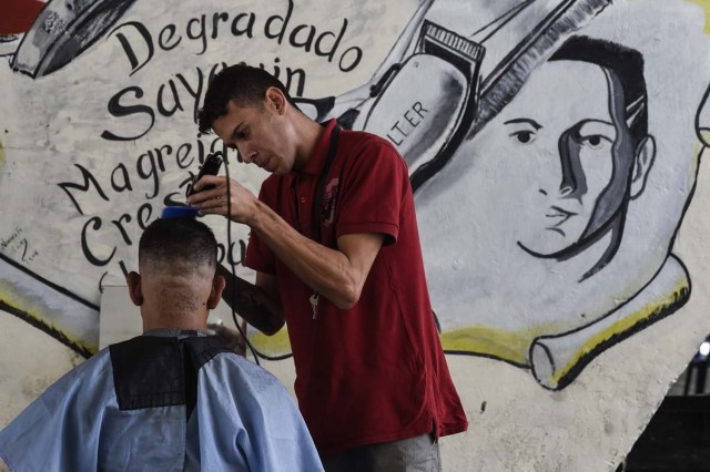 Un hombre trabaja cortando cabello bajo un puente en Caracas el 28 de mayo de 2018. Bajo un puente o en un mercado al aire libre en Caracas, los peluqueros se ganan la vida con herramientas simples y ofrecen cortes de pelo para aquellos que no pueden pagar un salón de belleza porque de la crisis económica. / AFP PHOTO / Juan BARRETO